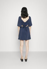 Granatowa mini sukienka z krótkimi bufkami, wycięciem na plecach oraz kokardą w talii. Gładki materiał i luźny krój.