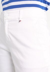 Bílé bavlněné kalhoty se slim fit, jemnou texturou a malou červenou, bílou a modrou akcentací blízko pásku.