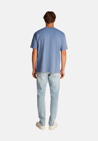 Camiseta de algodón azul claro con mangas cortas, escote redondo y corte relajado, combinada con jeans de mezclilla azul claro y zapatillas blancas.