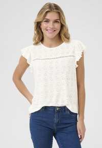 Haut blanc à manches courtes avec un motif brodé, des manches à volants et une bande décorative horizontale. Associé à un jean en denim bleu.
