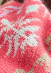 Ada mezgātā sega spilgti koraljkrāsā ar gaiši zilu un zaļu ģeometrisku rakstu. Mīksts, teksturēts vilnas audums ar sarežģītas šuves apdari.