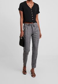 Czarny krótki top z guzikami, szare wąskie spodnie z wysokim stanem w paski z paskiem do wiązania, boczne kieszenie i czarne sandały na obcasie. W komplecie czarna torebka.