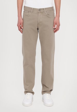 Beige tapered jeans med fem lommer, knaplukning og bæltestropper, kombineret med hvide sneakers. Stoffet ser glat og ensartet ud.