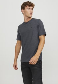 Mørkegrå t-shirt med korte ærmer lavet af blødt materiale, med en rund halsudskæring og et lille logo på brystet. Bæret med sorte jeans.
