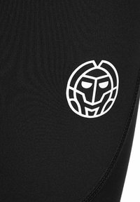 Leggings atléticos negros con un emblema blanco que presenta un diseño de cara estilizada en la parte inferior derecha. Textura suave con forma ajustada.