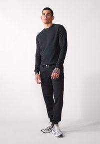 Schwarzer Pullover mit langen Ärmeln und rundem Halsausschnitt, kombiniert mit schwarzen Jogginghosen mit elastischem Bund und Kordelzug.