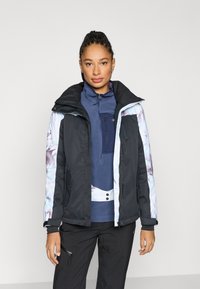 Melna un gaiši zila jaka ar rāvējslēdzēju, ar ziedu raksta piedurknēm, augstu apkakli un vairākām kabatām ar rāvējslēdzējiem. Valkāta kopā ar tumši zilu topu un biksēm.