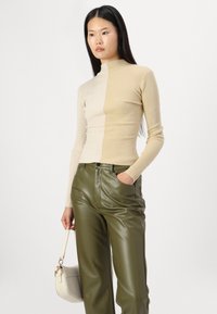 Pull à col roulé côtelé crème avec des manches longues, associé à un pantalon large en simili cuir vert olive. Présente une silhouette ajustée.