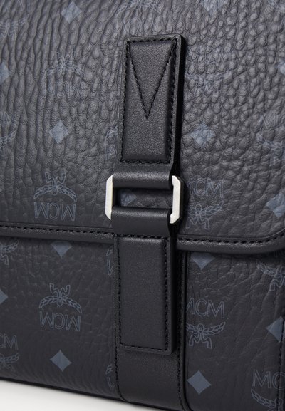 Borsa a tracolla in pelle nera strutturata con loghi MCM in rilievo e chiusura a fibbia in metallo argentato. Include una tracolla a contrasto.