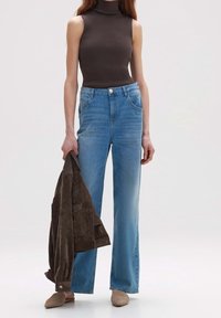 High-waisted light blue jeans with a straight leg, paired with a dark brown ribbed sleeveless top and a brown suede jacket. Beige mules.