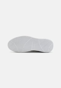 Semelle de chaussure en caoutchouc blanc avec un motif de dentelle en zigzag et le nom de la marque embossé au centre, présentée sur un fond léger uni.