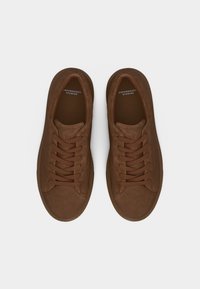 Ζευγάρι καφέ σουέτ αθλητικά παπούτσια με κορδόνια από το Copenhagen Studios, φωτογραφημένα από πάνω σε λευκό φόντο.