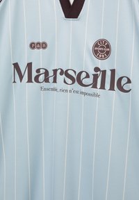 Hellblaues Sporttrikot mit weißen vertikalen Streifen, schwarzem Kragen, dem Schriftzug "Marseille", dem Logo "City Sports Club 1991" und einem französischen Motto darunter.
