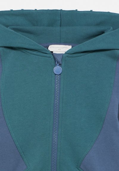 Green and blue children's hooded zip-up jacket with circular logo zipper pull and "Stella McCartney Kids" label inside collar.