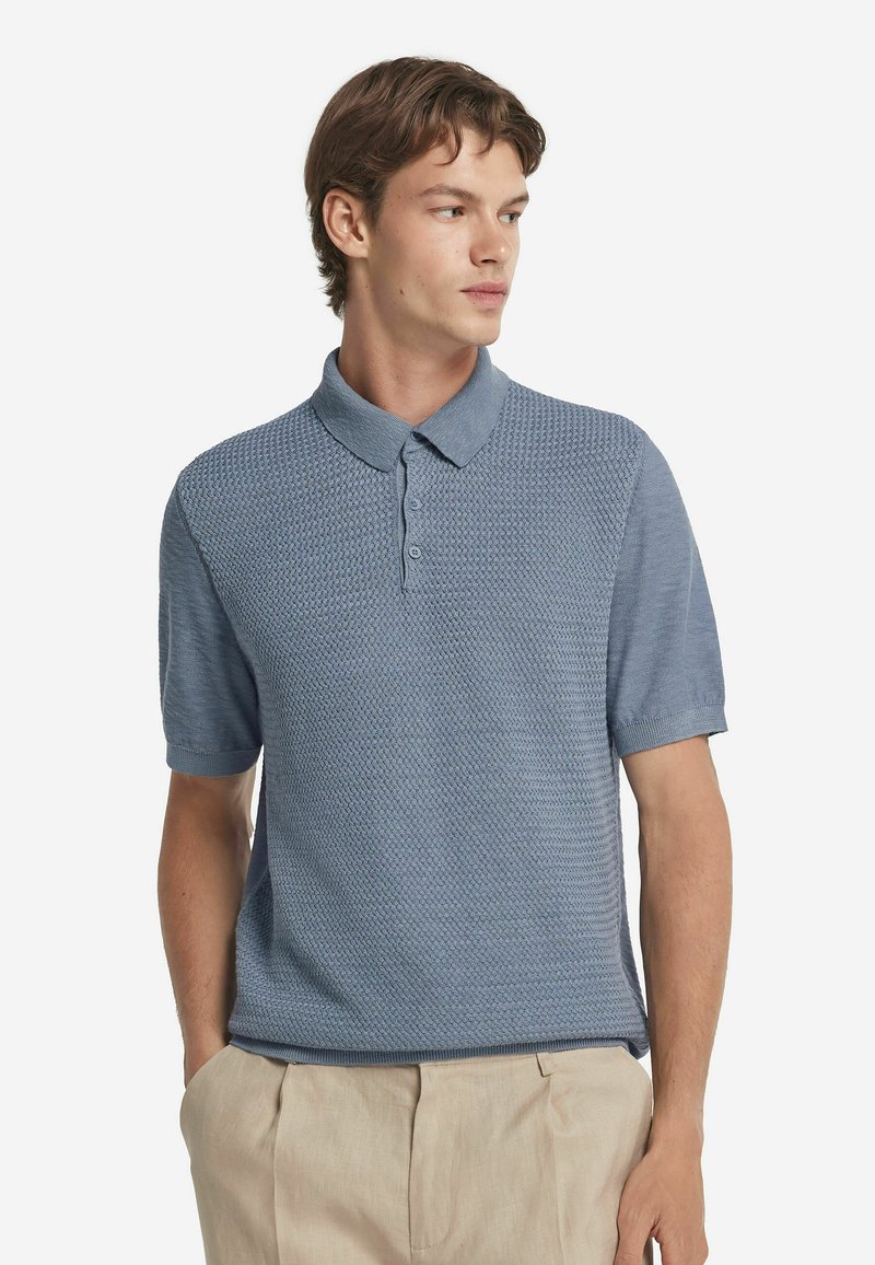 Kortärmad polo shirt i ljusblå, med strukturerad stickad mönster, med krage och tvåknapigt placket, kombinerad med beiga byxor.