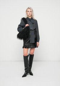 Mustapintainen, teksturoitu tekoturkishandbag, ruudullinen napitettava paita jousihenkäyksellä, musta nahkainen minihame rypytetyillä reunoilla ja polven korkuiset mustat korkokengät.