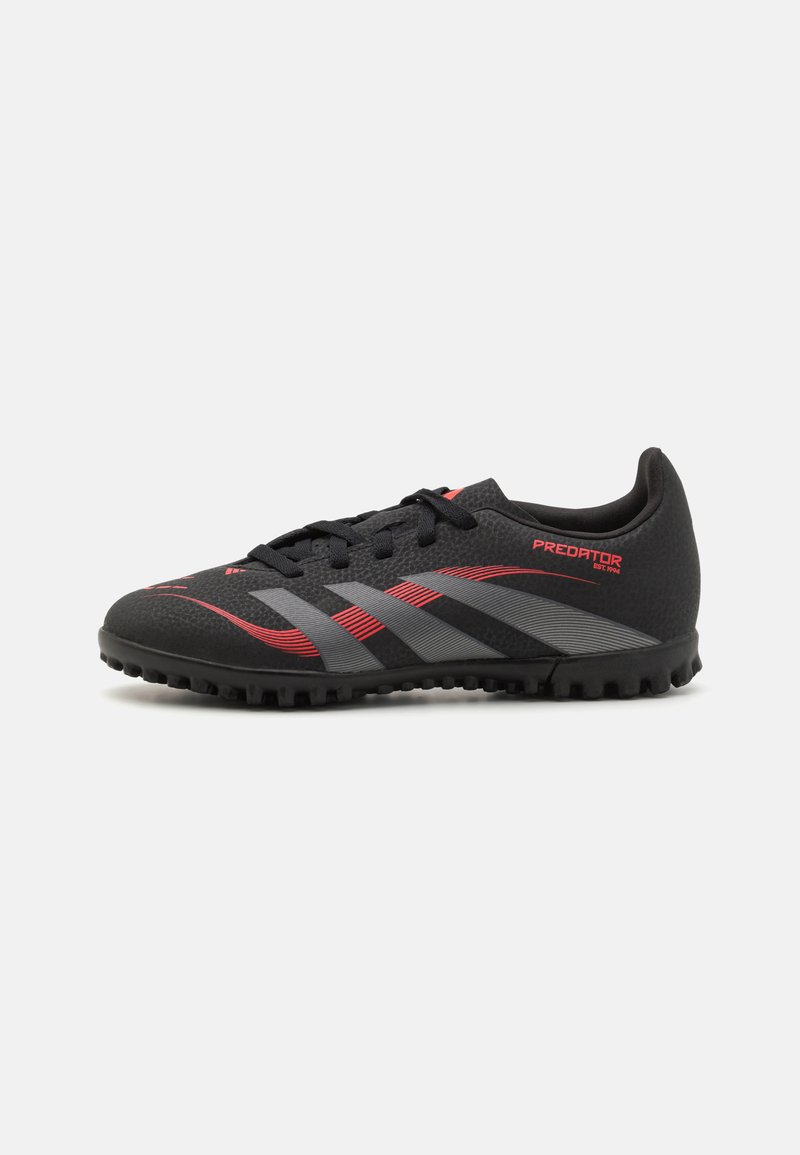 Chaussure de soccer noire avec tige en synthétique, surface texturée, bandes rouges et grises, et semelle rugged pour l'adhérence. Design léger et profil bas.