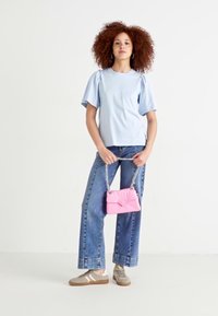 Haut bleu clair avec des manches bouffantes, jean bleu taille haute et baskets beiges. Sac à main rose avec une bandoulière en chaîne.