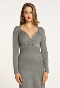 Grå, langærmet kjole med dyb V-udskæring, samlet detalje ved bodice og tætsiddende silhuet. Blødt strikstof med ribbet talje.
