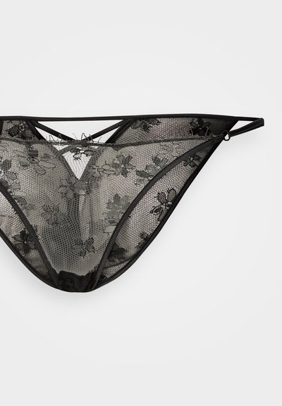 Tanga preta em renda com padrão floral, apresentando tule transparente, formato triangular, tiras elásticas e detalhe de fecho nas costas.