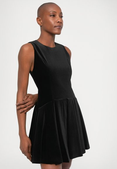 Zwarte fluwelen mouwloze jurk met een getailleerde bovenkant en een uitlopende geplooide rok. Gladde textuur met een ronde halslijn en geen zichtbare sluitingen.