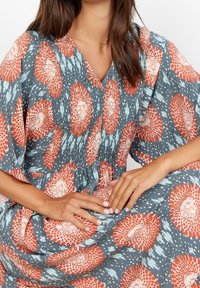 Blumenkleid mit blauem Hintergrund, großen roten und weißen Blüten, kurzen Ärmeln und gerafften Details am Oberteil.