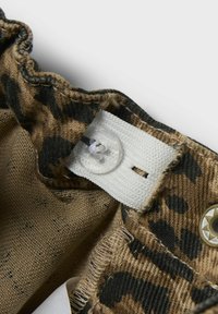 Bomuldsbeklædningsgenstand med leopardmønster i nuancer af brun og sort. Har en hvid rem og klar knaplukning.