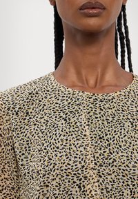 Ľahká, vzorovaná blúzka s okrúhlym výstrihom a rôznymi čiernymi a žltými bodkami na béžovom pozadí; hladká textúra.