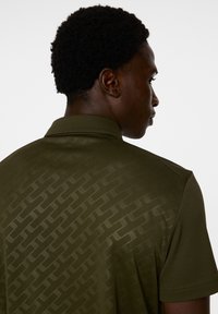 Oliwkowa koszulka polo z subtelnym, teksturowanym wzorem, krótki rękaw i kołnierz. Gładki materiał i dopasowany krój.