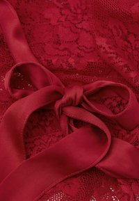 Czerwona koronka z gładką satynową wstążką. Koronka ma misterny, kwiatowy wzór, a wstążka to jednolita, głęboka czerwona satynowa taśma.