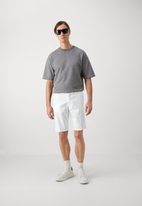 Camisa gris de manga corta, pantalones cortos blancos, gafas de sol y zapatillas blancas. Diseño simple y limpio con un ajuste relajado. Textura de tela suave.