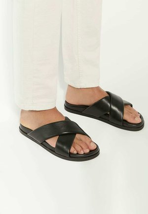 Black slide sandals with crossed straps, made of smooth leather. Flat sole, minimal design, features open toe and side foot exposure.