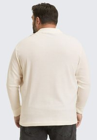 Langermige, crèmekleurige polo met een gestructureerde stof en een klassieke kraag, gedragen met donkergrijze jeans.