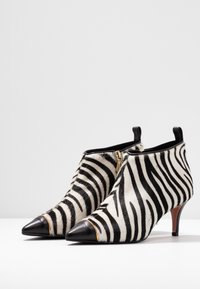 Zebra print enkellaarsjes met een zachte bonttextuur, zwarte leren spitse neus, gouden ritsdetails en een slanke hak.