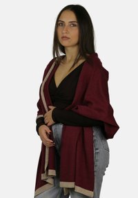 Burgundowy szal ze złotym wykończeniem, lekka tkanina, swobodnie narzucony. Noszony na ciemnej bluzce, w połączeniu z jasnymi jeansami.