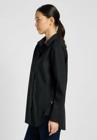 Zwarte button-up shirt van lichtgewicht stof, voorzien van een klassieke kraag, lange mouwen en een gebogen zoom. Eenvoudig ontwerp zonder zichtbare patronen.