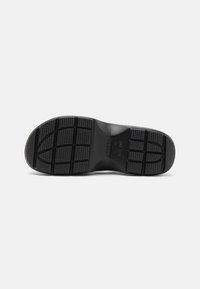 Semelle de chaussure en caoutchouc noir présentant un motif de semelle avec des carrés texturés et des rainures pour une meilleure adhérence. Design à bout arrondi et talon plat.