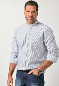 Camicia da uomo con bottoni, caratterizzata da righe verticali blu e bianche, collo alla coreana e maniche lunghe, indossata con jeans scuri e un orologio.