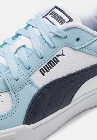 Világoskék és fehér sportcipő nubuk és bőr textúrákkal. Kék fűzőkkel, gumitalppal és fekete Puma logóval az oldalon.