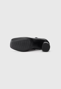 Black high-heeled shoe sole featuring a textured rubber grip and a contoured design with visible tread lines for traction.