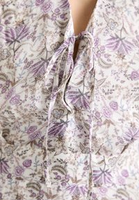 Floral blouse with lightweight fabric, featuring a purple and cream color scheme, delicate tie closure, and intricate floral patterns.