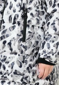 Chaqueta acolchada en estampado de animal en blanco y negro, con cierre de cremallera y puños acanalados para mayor calidez. Textura lisa y brillante.