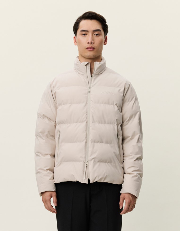 Casaco puffer bege com gola alta, design quilted horizontal, fecho de zíper e dois bolsos frontais, feito de material leve e suave.