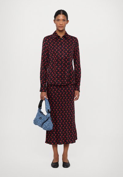 Top și fustă cu model negru și forme de semilună roșii. Modelul ține o geantă albastră deschisă cu un mâner negru. Pantofii plat negru completează look-ul.