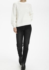 Biały długi sweter dzianinowy z textured wzorami, z okrągłym dekoltem i ściągaczami, w połączeniu z dopasowanymi czarnymi dżinsami i czarnymi szpiczastymi botkami.