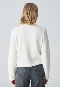 Hvid, fluffy striktrøje med en løs pasform, ribbede ærmer og en rund halsudskæring, parret med mørkegrå højtaljede jeans.