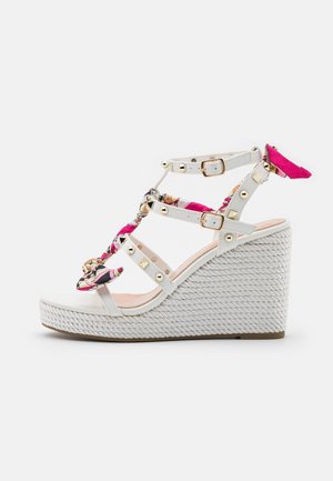 Witte sleehak sandalen met gevlochten bloemenaccenten en gouden studs. Beschikt over een geweven zool en verstelbare bandjes voor een veilige pasvorm.