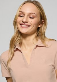 Jasnoróżowa koszulka polo o miękkiej fakturze, z kołnierzykiem i subtelnym logiem "POLO CLUB" na piersi.