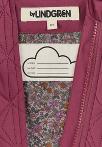 Violet vuorattu vaate sisäpuolella, jossa on kukkakuosiset vuorikangas. Tagi lukee "by LINDGREn" ja siinä on tilaa lasten nimille. Vetoketjukiinnitys.