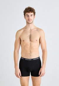Schwarze Boxershorts aus weichem Material mit einem Markenbund in weißer Schrift. Die Passform liegt eng am Körper an und hat eine glatte Textur.